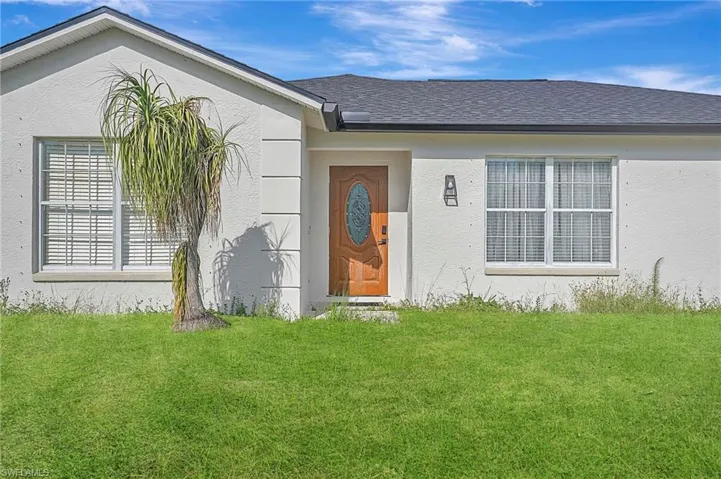 Entrance to property with a lawn, stucco siding, and roof with shingles