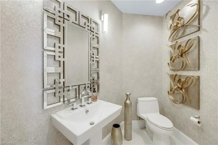 The powder room has a modern vibe with a custom mirror, lighting and wallpaper.