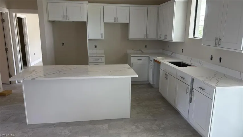 Kitchen featuring a center island, white cabinetry, and light stone counters