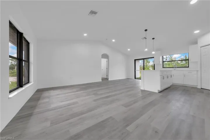 Unfurnished living room featuring arched walkways, vaulted ceiling, recessed lighting, and light wood finished floors