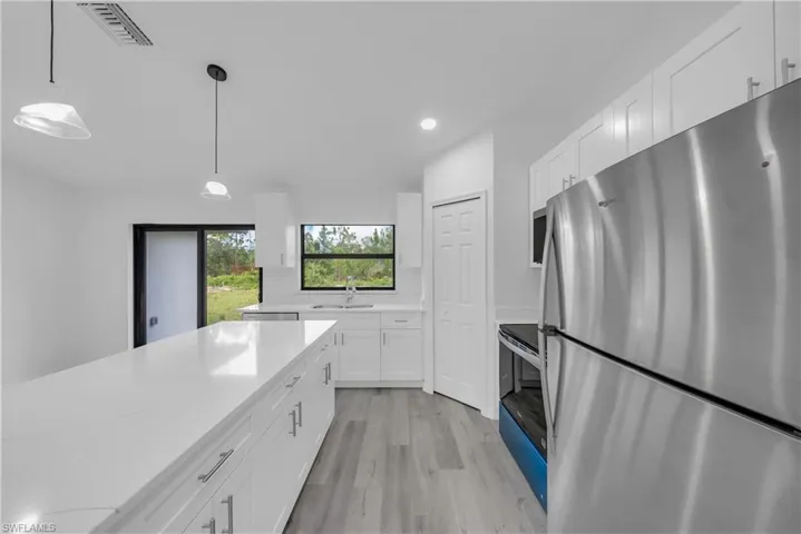 Kitchen with stainless steel appliances, white cabinets, light wood-style flooring, and light stone countertops