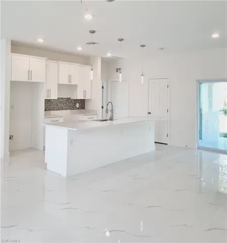 Kitchen with pendant lighting, a large island, white cabinetry, and sink