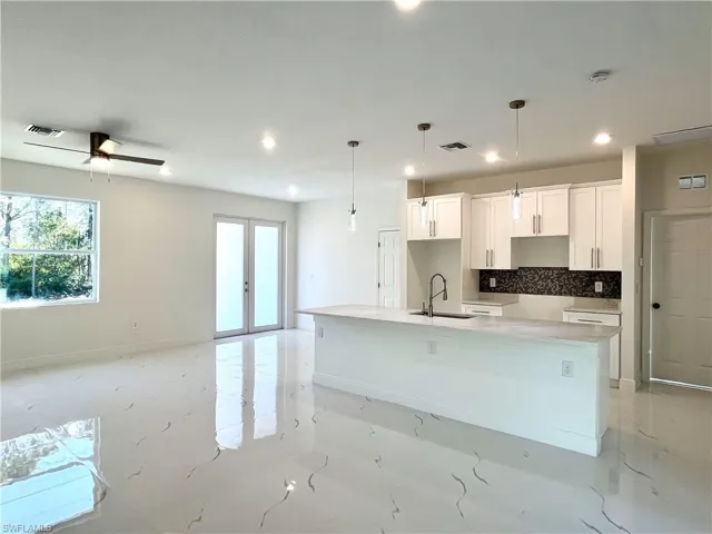 Kitchen featuring pendant lighting, a spacious island, sink, tasteful backsplash, and white cabinetry