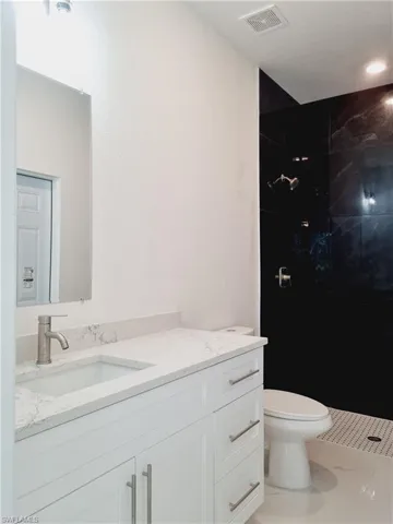 Bathroom with tile patterned flooring, vanity, toilet, and a tile shower