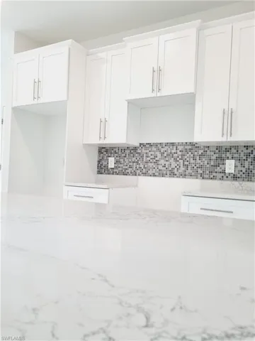 Kitchen featuring backsplash, white cabinetry, and light stone counters