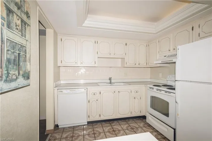 Kitchen with a tray ceiling, white appliances, backsplash, sink, and ornamental molding