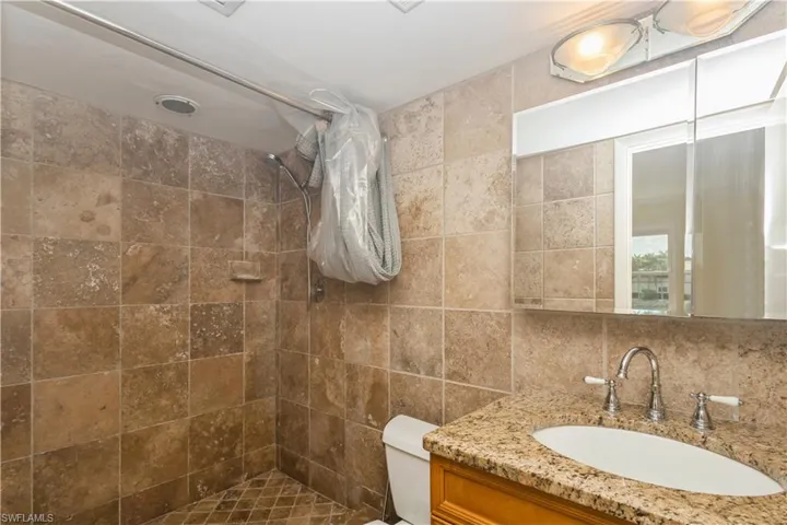 master Bathroom featuring a tile shower, oversized vanity, toilet, and tile walls
