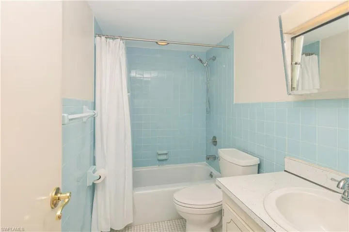 Full bathroom with tile flooring, tile walls, shower / tub combo with curtain, toilet, and large vanity