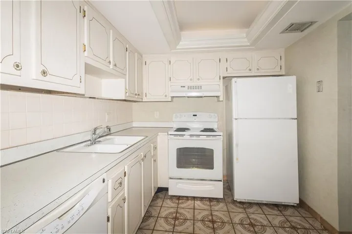 Kitchen featuring a tray ceiling, white appliances, backsplash, sink, and white cabinets