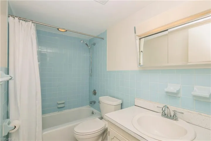Full bathroom with tile walls, oversized vanity, toilet, tasteful backsplash, and shower / tub combo with curtain