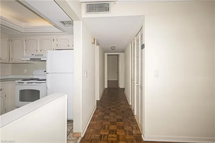 Kitchen featuring dark parquet flooring, white appliances, and white cabinetry