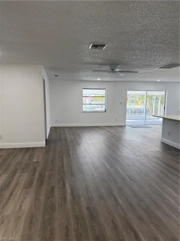 Empty room with dark wood finished floors, ceiling fan, and a textured ceiling