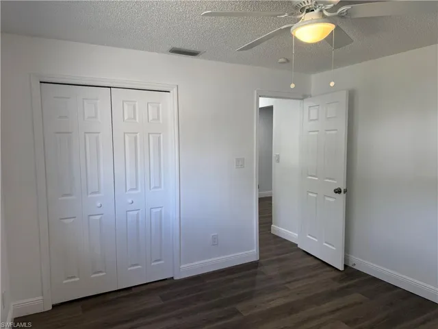 Unfurnished bedroom featuring a textured ceiling, ceiling fan, dark wood-style floors, and a closet