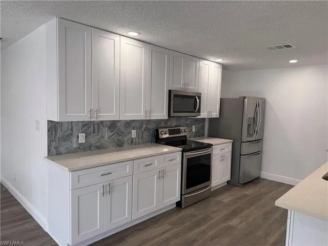 Kitchen featuring stainless steel appliances, backsplash, white cabinets, a textured ceiling, and recessed lighting