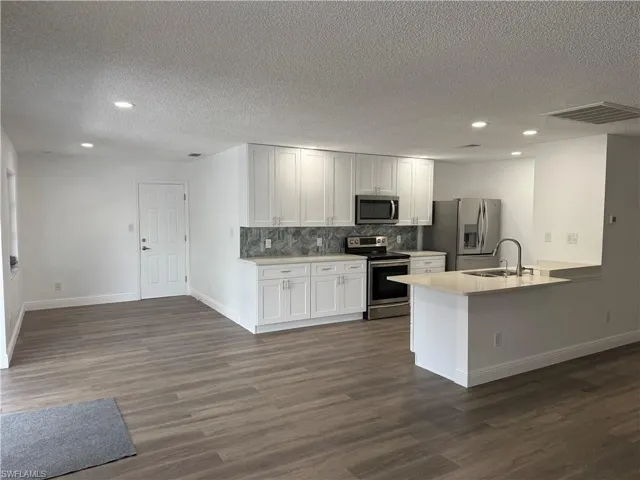 Kitchen featuring recessed lighting, stainless steel appliances, backsplash, a peninsula, and dark wood finished floors