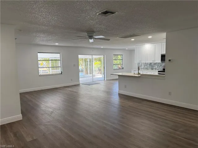 Unfurnished living room with a textured ceiling, plenty of natural light, a ceiling fan, recessed lighting, and dark wood-style flooring