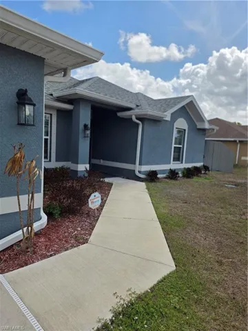 Property entrance featuring stucco siding, a shingled roof, and a yard