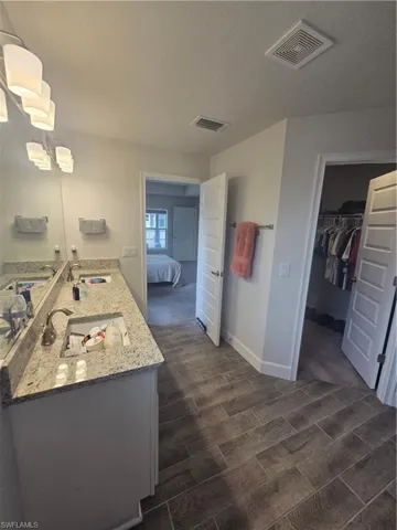 Ensuite bathroom with double vanity, a spacious closet, and wood tiled floors