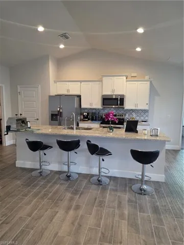 Kitchen with a kitchen bar, white cabinets, light stone counters, a spacious island, and stainless steel fridge