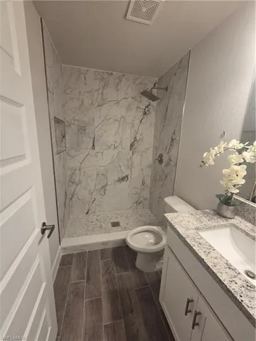 Bathroom featuring vanity, a marble finish shower, wood tiled floors, and a textured wall