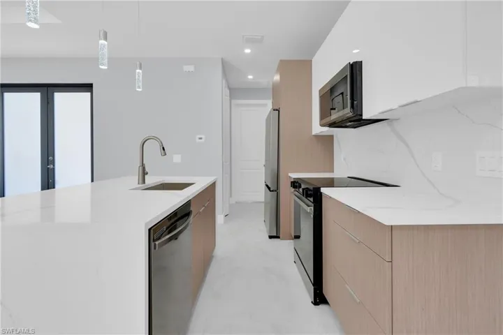 Kitchen featuring modern cabinets, light stone countertops, stainless steel appliances, and a kitchen island with sink