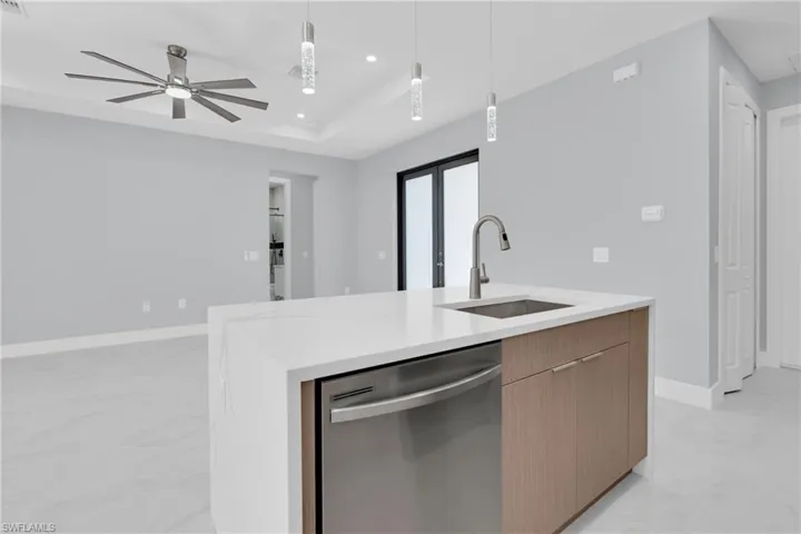 Kitchen with a center island with sink, dishwasher, light stone countertops, modern cabinets, and pendant lighting