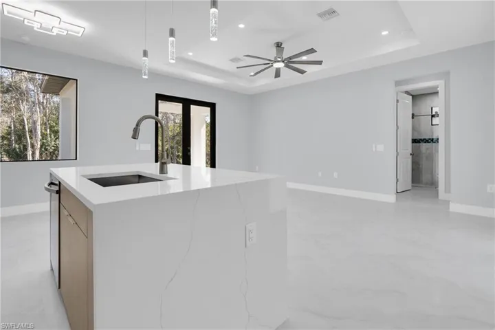 Kitchen featuring light stone counters, modern cabinets, pendant lighting, a kitchen island with sink, and ceiling fan
