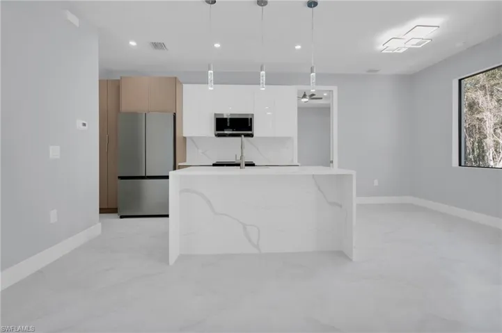 Kitchen featuring stainless steel appliances, decorative light fixtures, light stone counters, modern cabinets, and light marble finish flooring