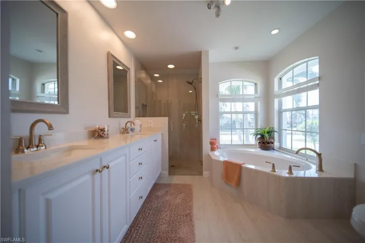 Full bathroom with double vanity, a garden tub, a shower stall, recessed lighting, and light wood finished floors