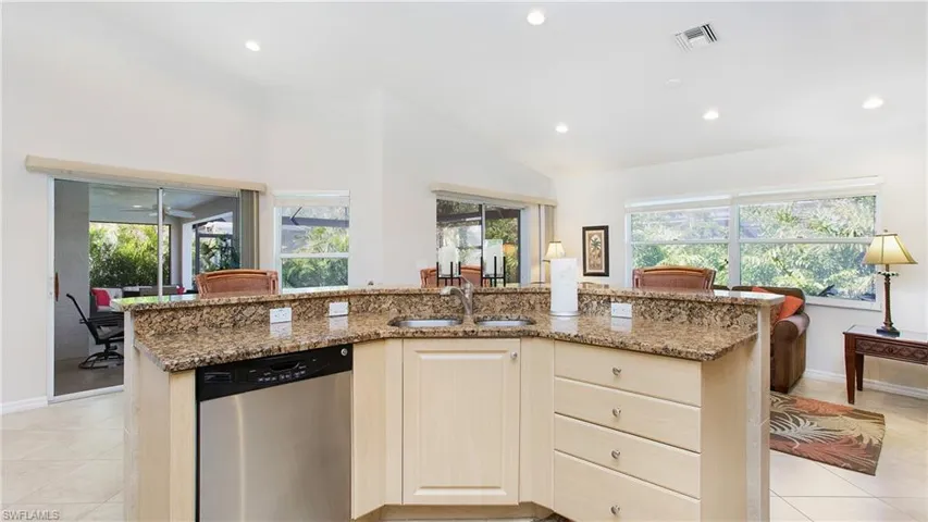 Kitchen with stainless steel dishwasher, light tile patterned floors, an island with sink, light stone counters, and recessed lighting