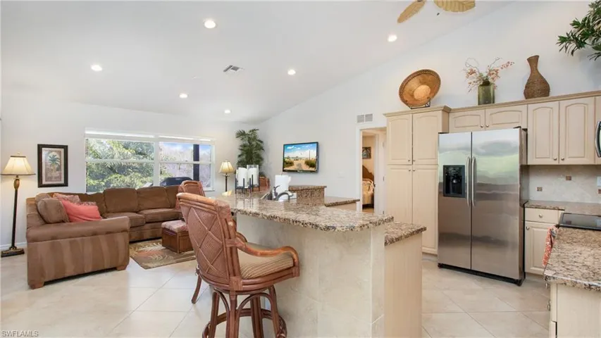 Kitchen with stainless steel refrigerator with ice dispenser, a breakfast bar, open floor plan, lofted ceiling, and recessed lighting