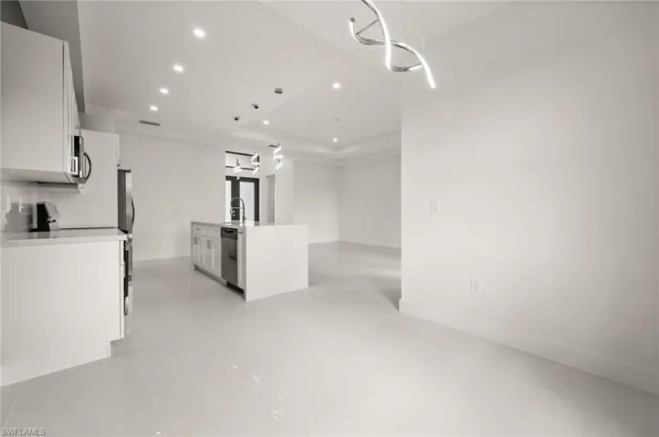 Kitchen with a kitchen island with sink, white cabinetry, stainless steel appliances, recessed lighting, and a tray ceiling