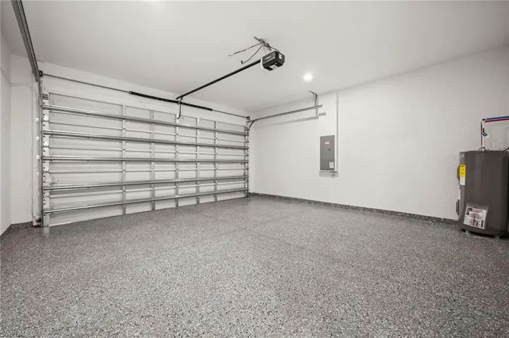 Garage with electric water heater, electric panel, and a garage door opener