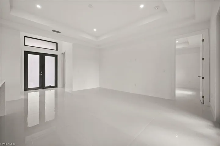 Empty room with french doors, a raised ceiling, recessed lighting, and light tile patterned floors