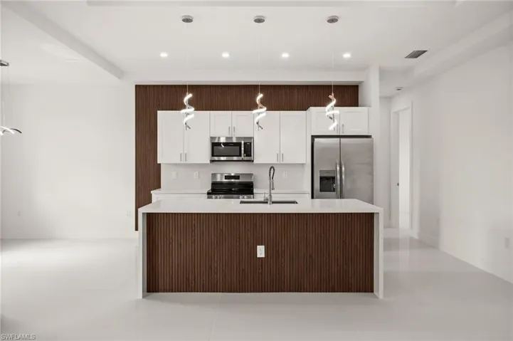 Kitchen with stainless steel appliances, an island with sink, white cabinetry, and light stone countertops