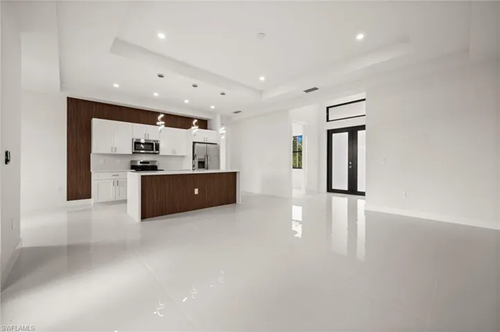 Kitchen with open floor plan, french doors, an island with sink, stainless steel appliances, and white cabinets