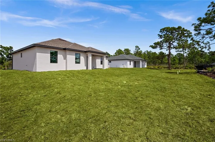 Back of property with stucco siding, a lawn, and roof with shingles