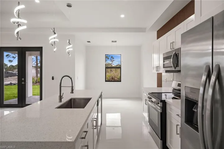 Kitchen with stainless steel appliances, a center island with sink, and light stone counters