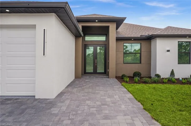 Property entrance with a shingled roof, stucco siding, french doors, a garage, and a yard