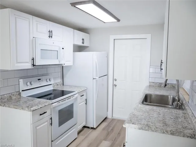 Kitchen with sink, white appliances, and white cabinetry