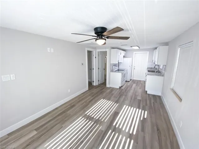 Unfurnished living room featuring wood-type flooring, sink, and ceiling fan