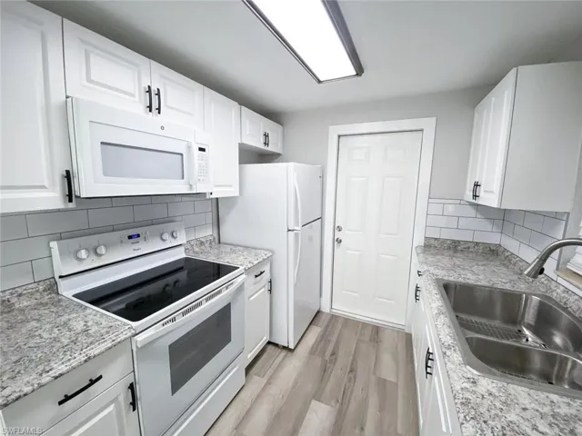 Kitchen featuring backsplash, white cabinetry, light wood-type flooring, sink, and white appliances