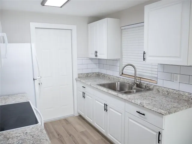 Kitchen featuring light hardwood / wood-style floors, tasteful backsplash, range, white cabinets, and sink