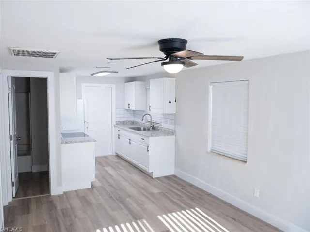 Kitchen with light hardwood / wood-style floors, white cabinets, sink, tasteful backsplash, and ceiling fan