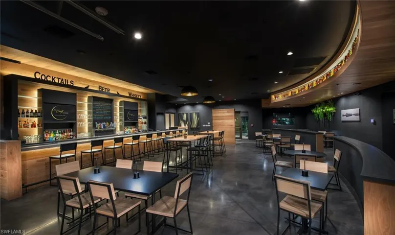 Spacious commercial interior featuring a full-service bar with under-cabinet lighting, wood-finish walls, and a curved display shelf