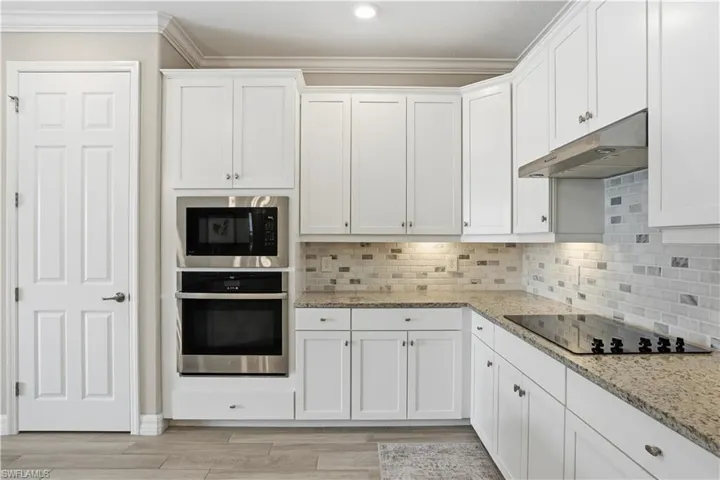 Kitchen with white cabinets, stainless steel appliances, light stone counters, crown molding, and decorative backsplash