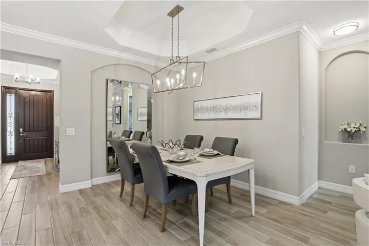 Dining room featuring hanging lights, wood tiled floors, ornamental molding, arched walkways, and a raised ceiling