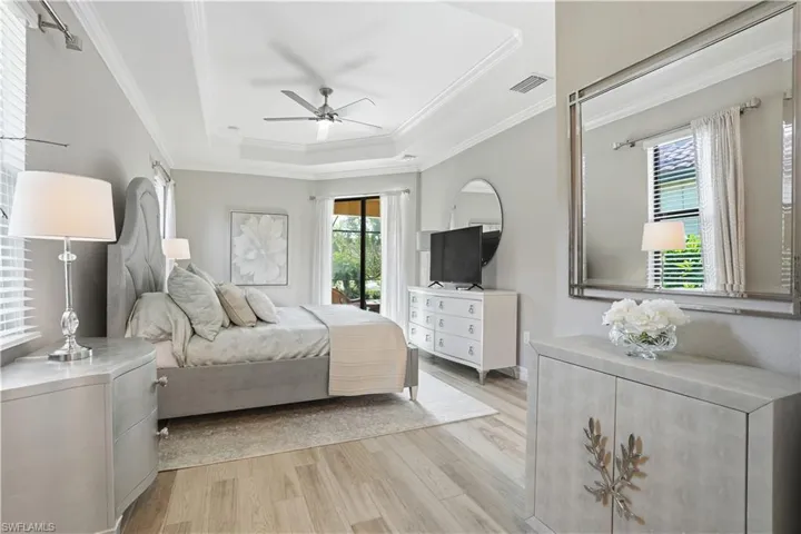 Bedroom featuring light wood-style floors, ceiling fan, access to exterior, a tray ceiling, and ornamental molding