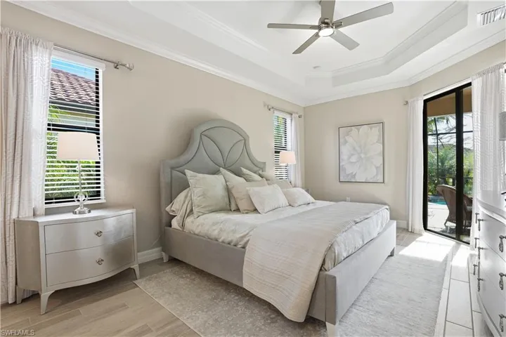 Bedroom featuring access to outside, a raised ceiling, multiple windows, light wood-style flooring, and ornamental molding