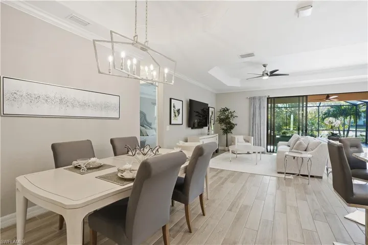 Dining area featuring light wood-style flooring, crown molding, a tray ceiling, ceiling fan, and suspended lighting